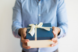 Mężczyzna podaje ładnie zapakowany prezent, kolory odcienie niebieskiego i beżu.